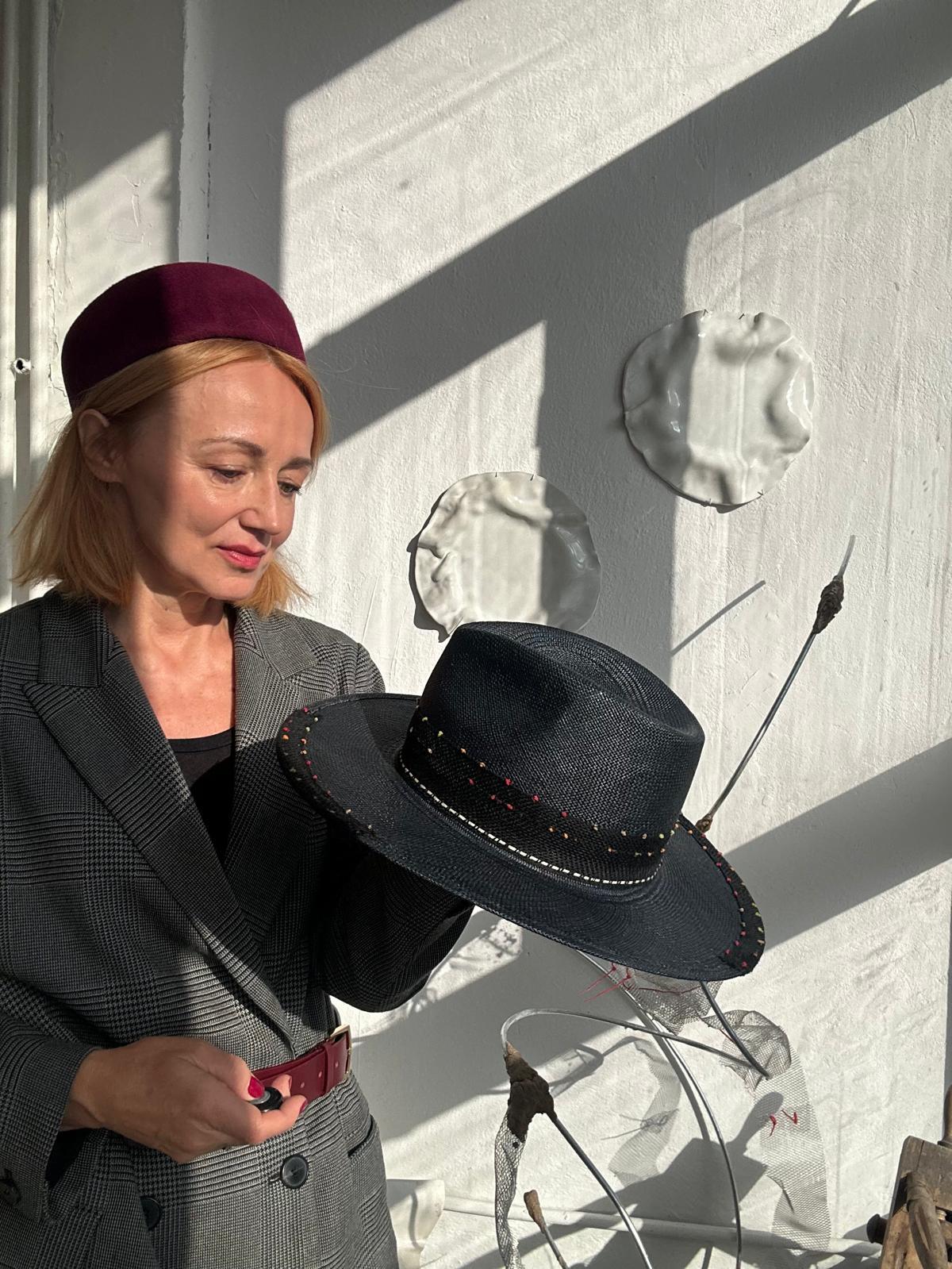 Woman in a burgundy pillbox holding a black straw fedora with a contrast stitched brim