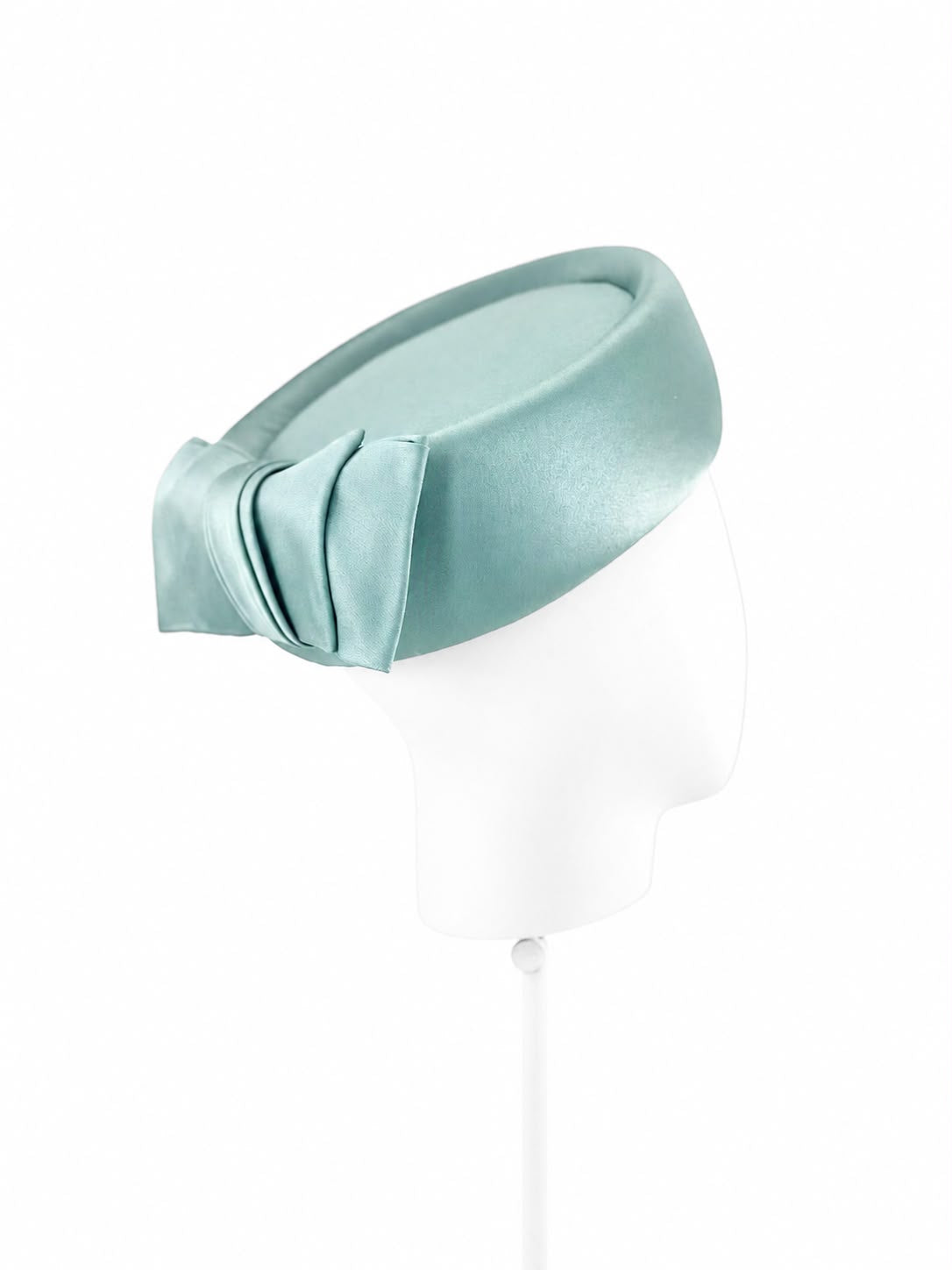 Celadon silk satin pillbox hat with a pleated bow, on a white display head, Maria Monica London