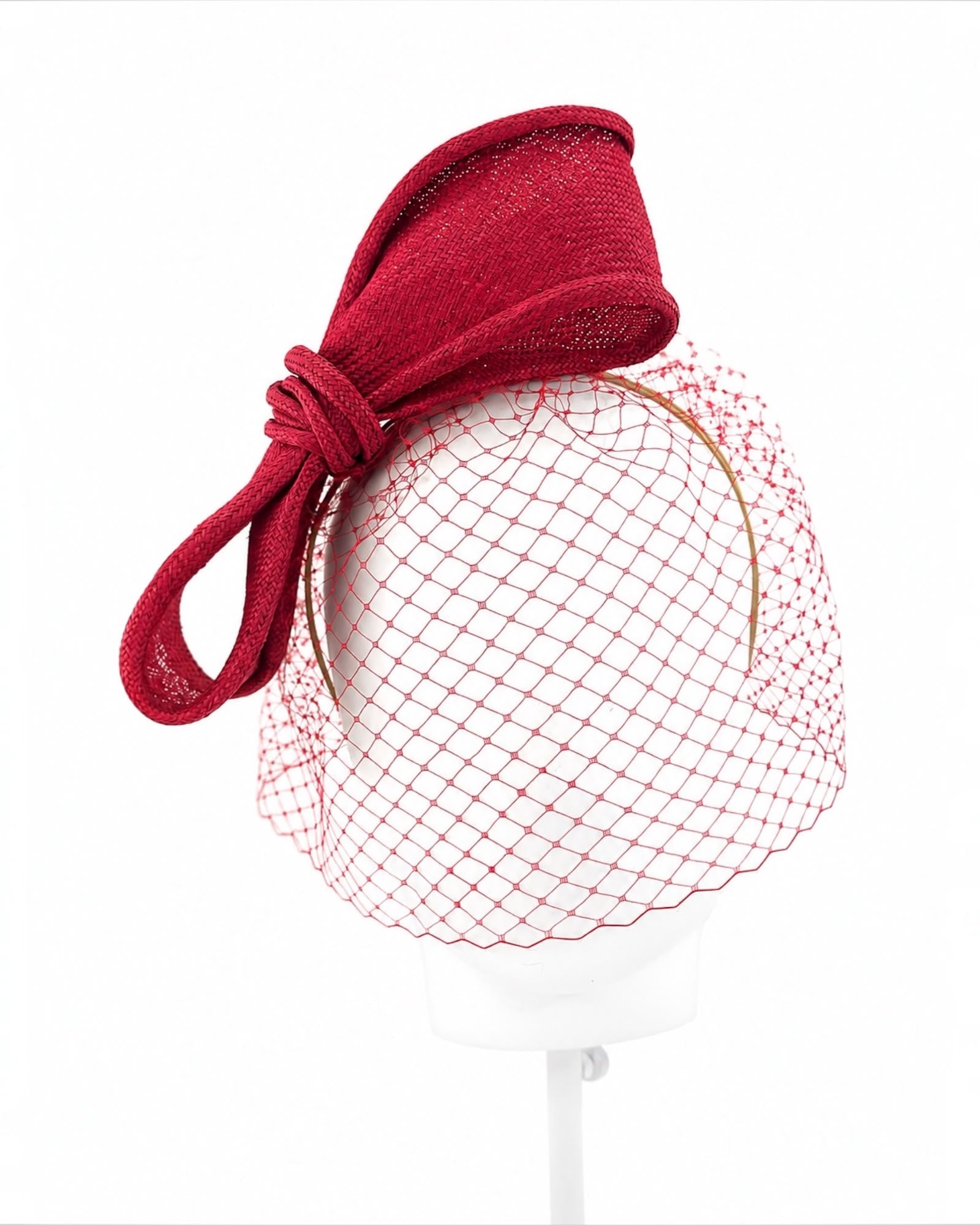 Crimson parasisal straw bow headpiece with a matching crimson face veil, shown on a display head, Maria Monica London