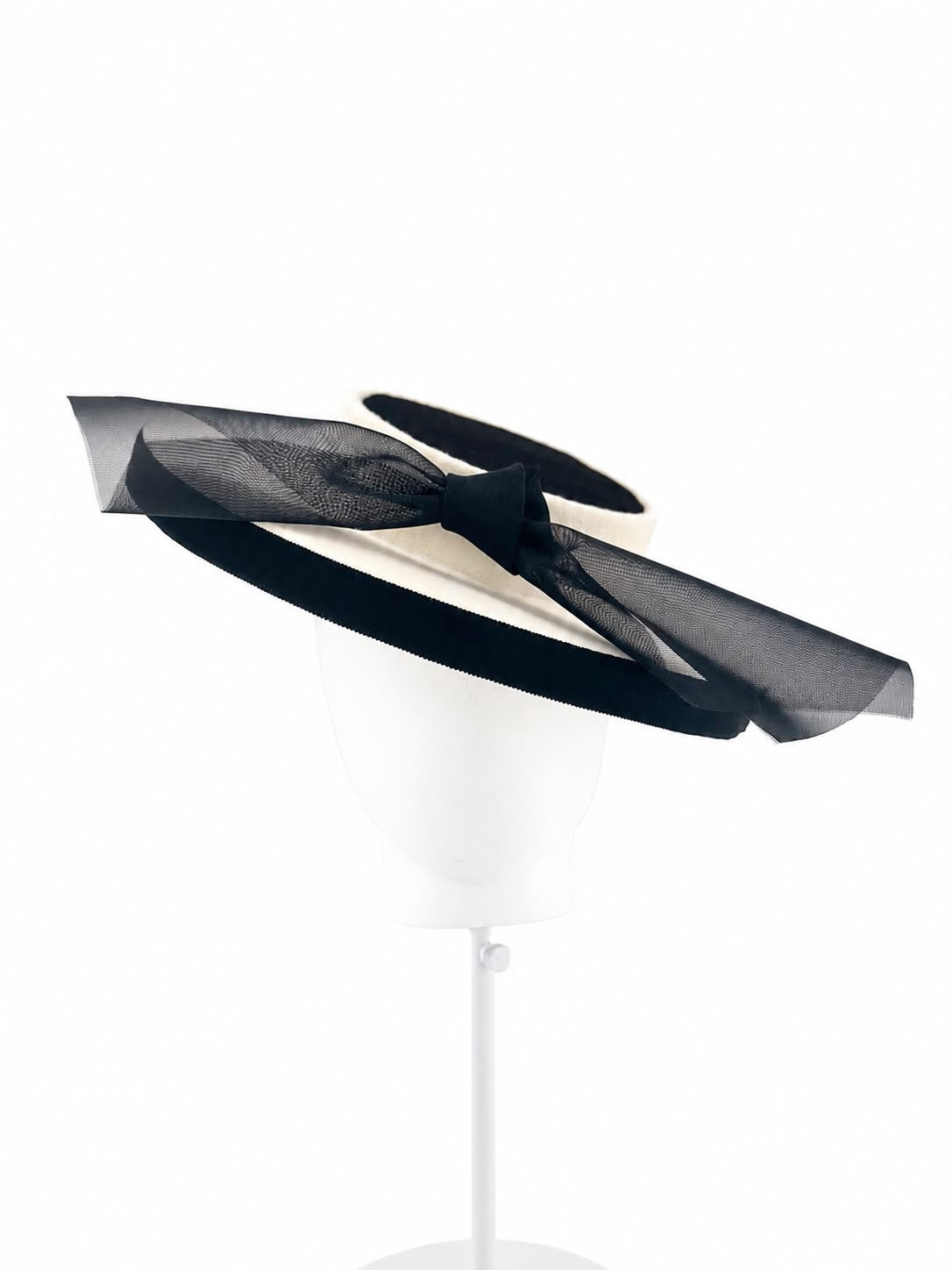 Ivory felt boater with a black grosgrain brim edge and a long black crinoline bow, worn at an angle on a display head, Maria Monica London