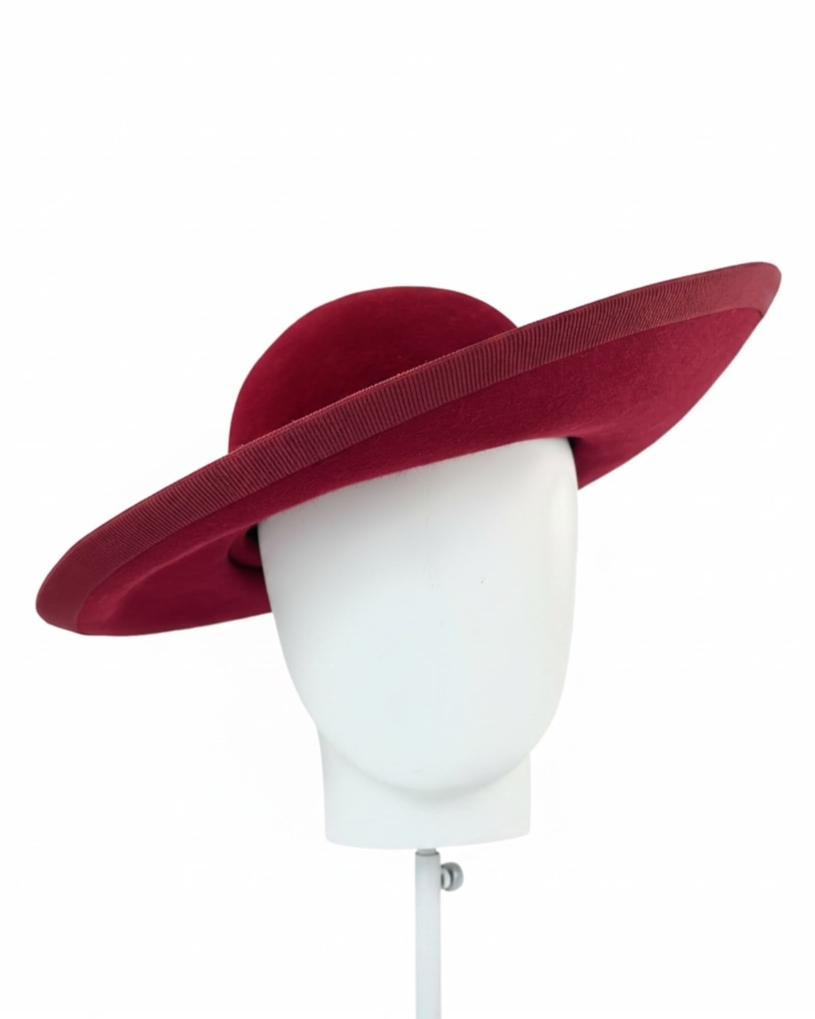 Deep burgundy asymmetric felt hat shown on a display head with the brim lifting away from the face, race day hat handmade in London