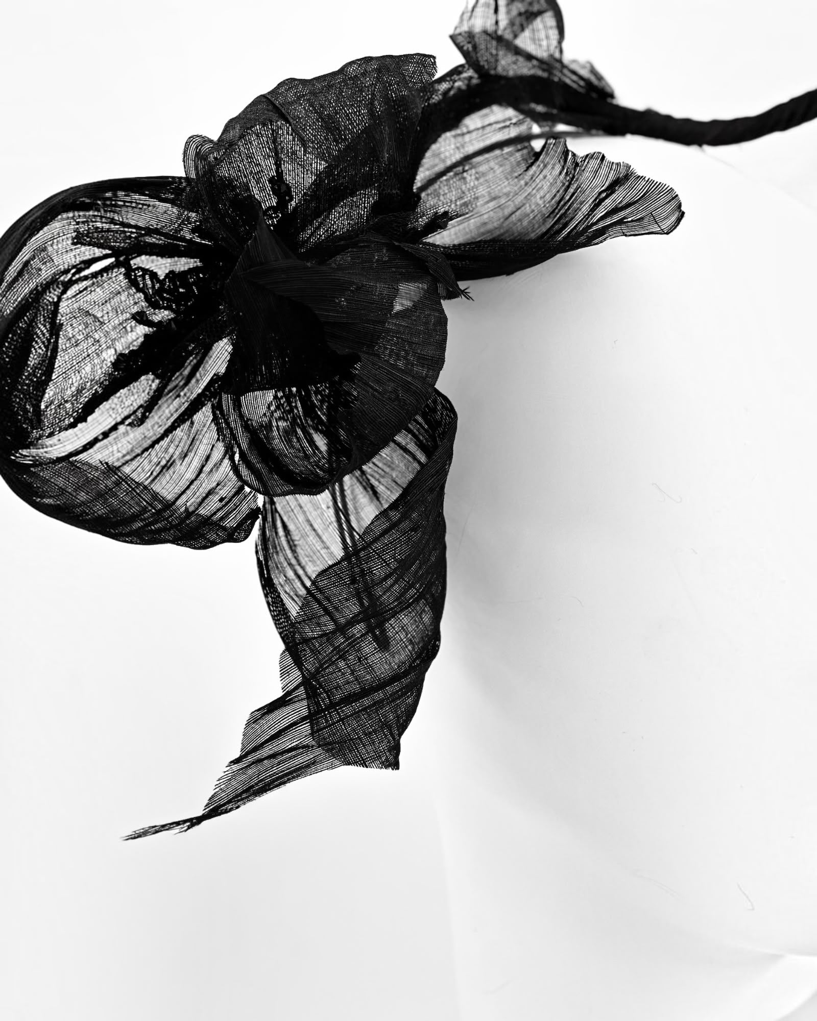 Close view of a black abaca flower headpiece, sheer pleated petals shaped around a folded centre, Maria Monica London