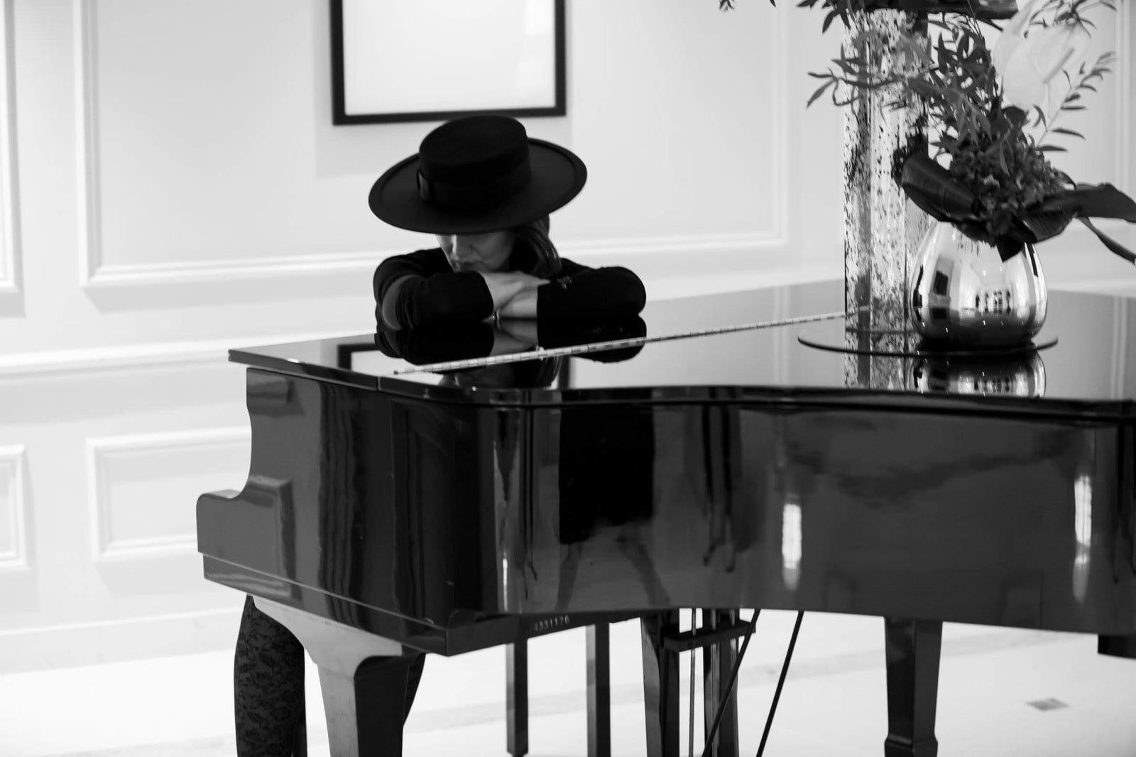 A black occasion hat resting on a grand piano, handmade in London by couture milliner Maria Monica London