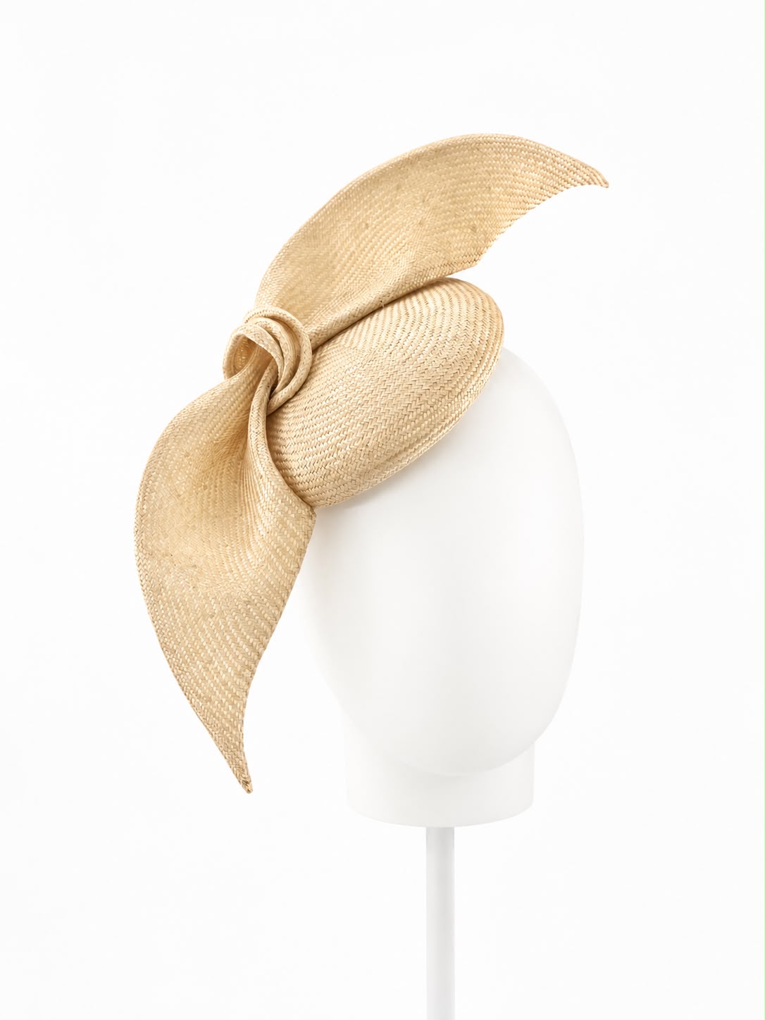 Champagne straw cocktail hat with a large sculpted straw bow, shown on a display head, Maria Monica London
