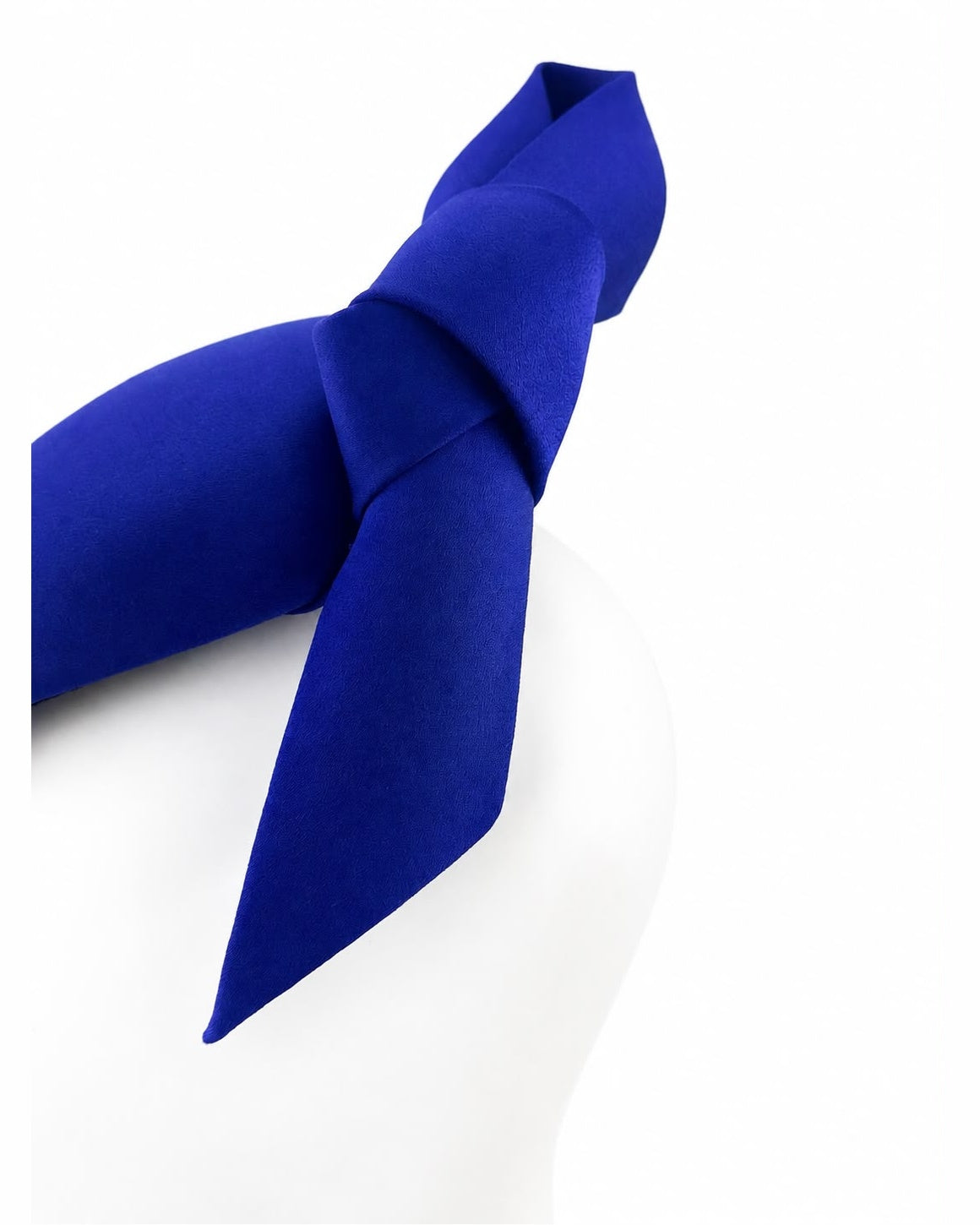 Close view of the hand-modelled satin knot sweeping to one side on the cobalt blue cocktail hat by a couture milliner