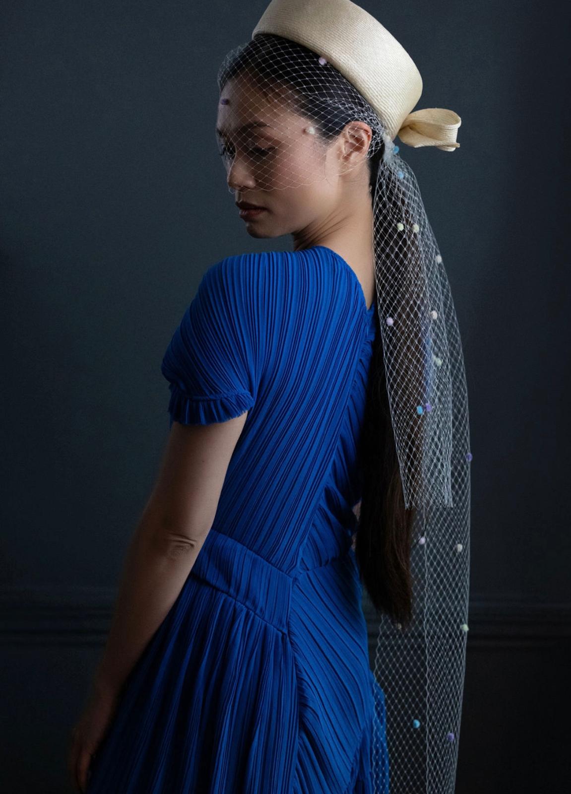 Cream straw pillbox with a long spotted veil, worn with a cobalt blue pleated dress, Maria Monica London