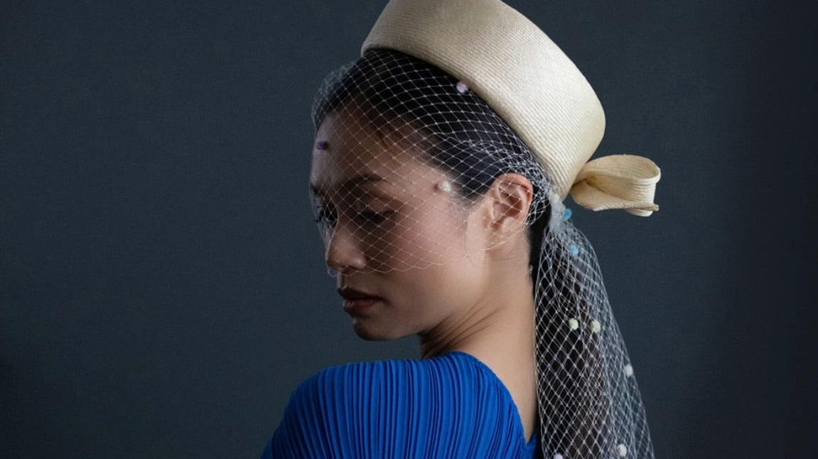 Cream straw pillbox with a long spotted veil worn in profile with a cobalt pleated top, Maria Monica London