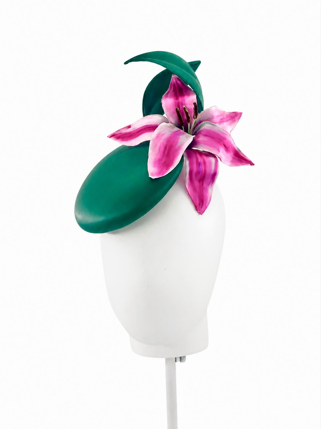 Emerald green cocktail hat with sculpted leaves and a pink lily, shown on a display head, Maria Monica London
