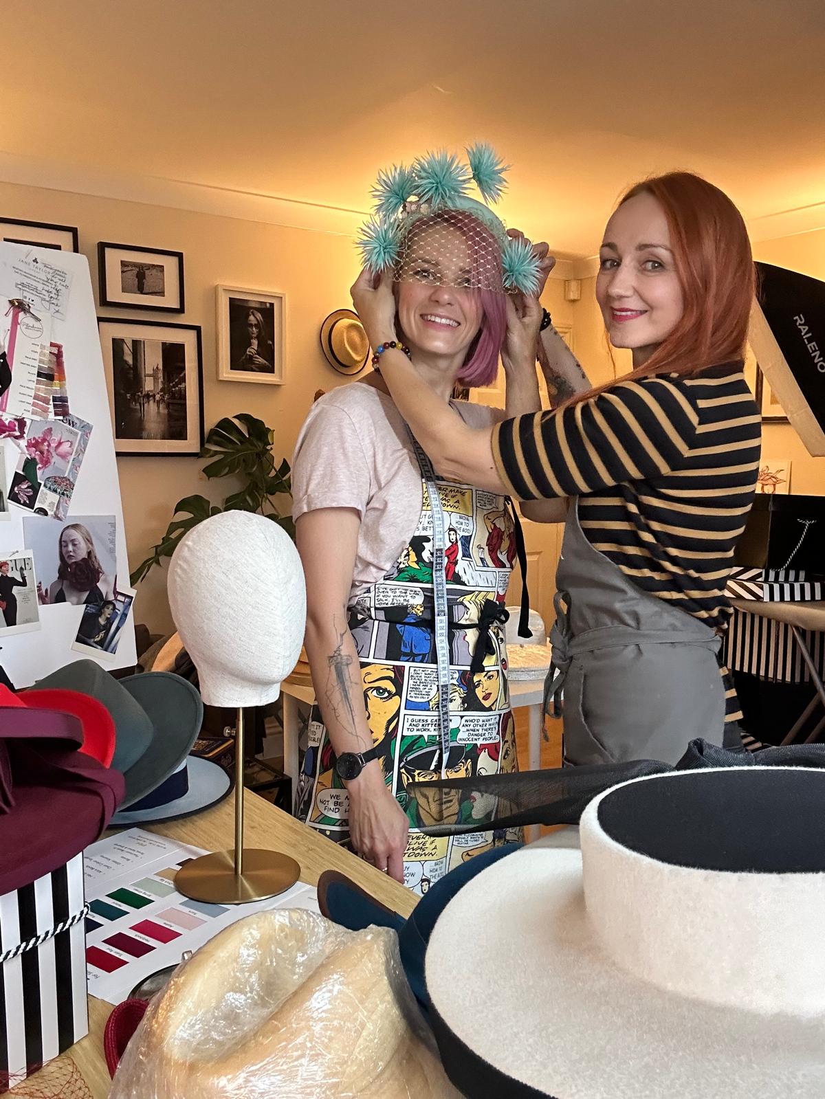 Fitting a mint pompom headpiece with veiling in a millinery studio, felt hats and colour swatch cards nearby