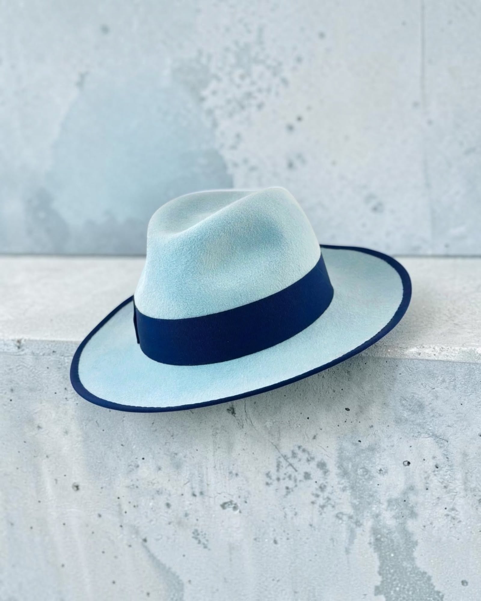 Front view of the ice blue felt fedora showing the pinched crown and the deep navy grosgrain band, handmade in London