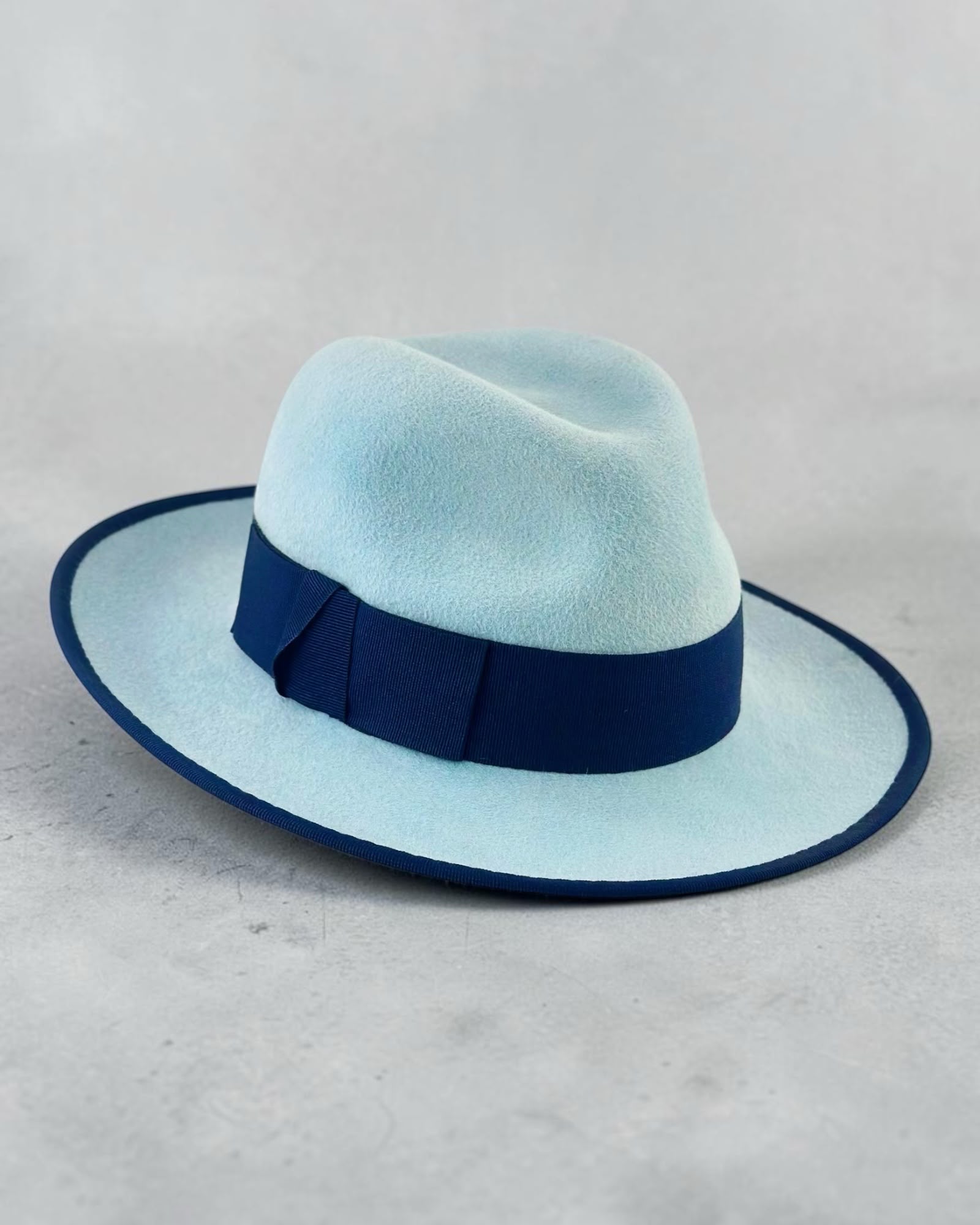 Side view of the ice blue felt fedora showing the navy bound brim line, couture millinery handmade in London