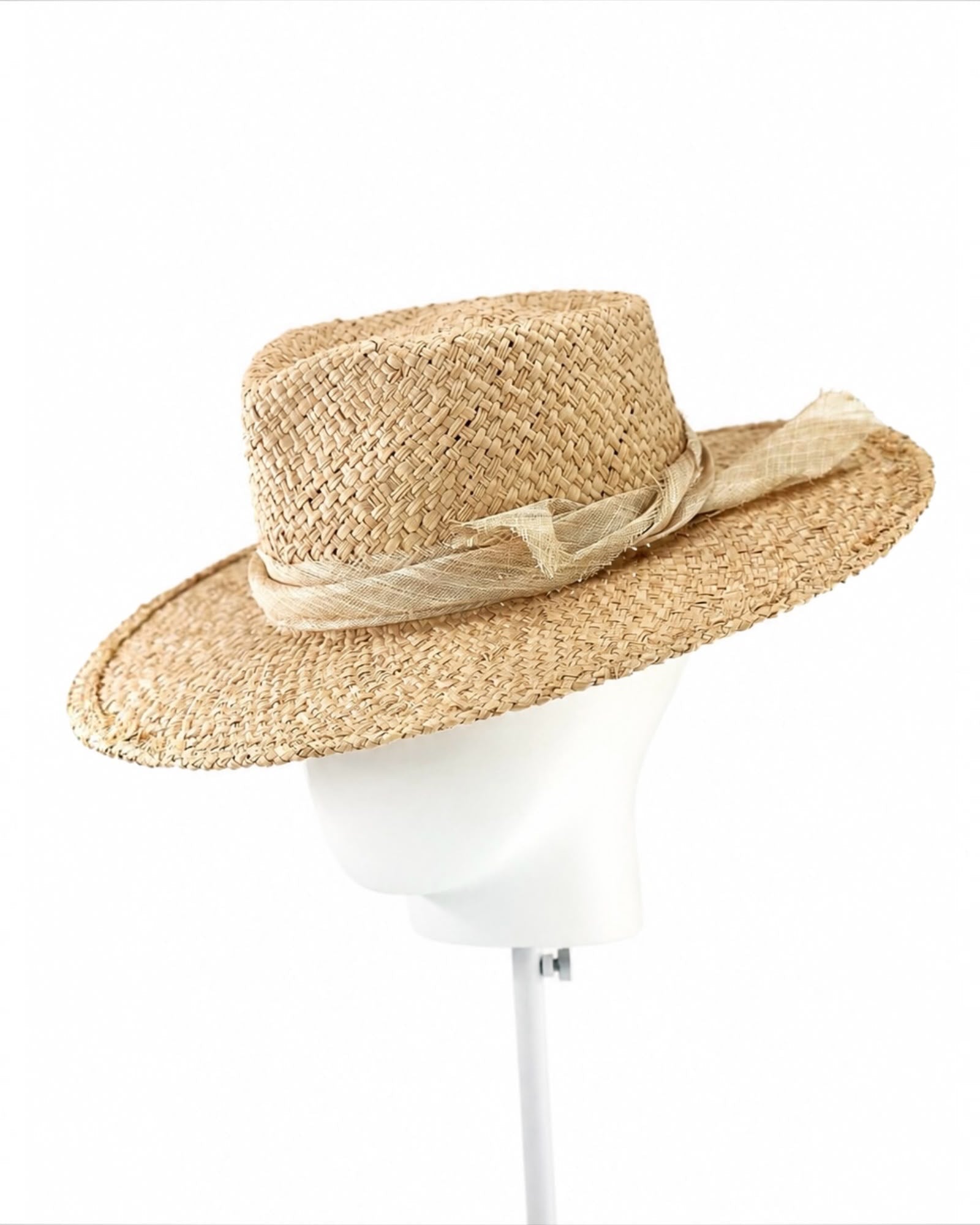 Natural sand raffia fedora with a wide upturned brim and trailing pinokpok bow, shown on a white display head, Maria Monica London
