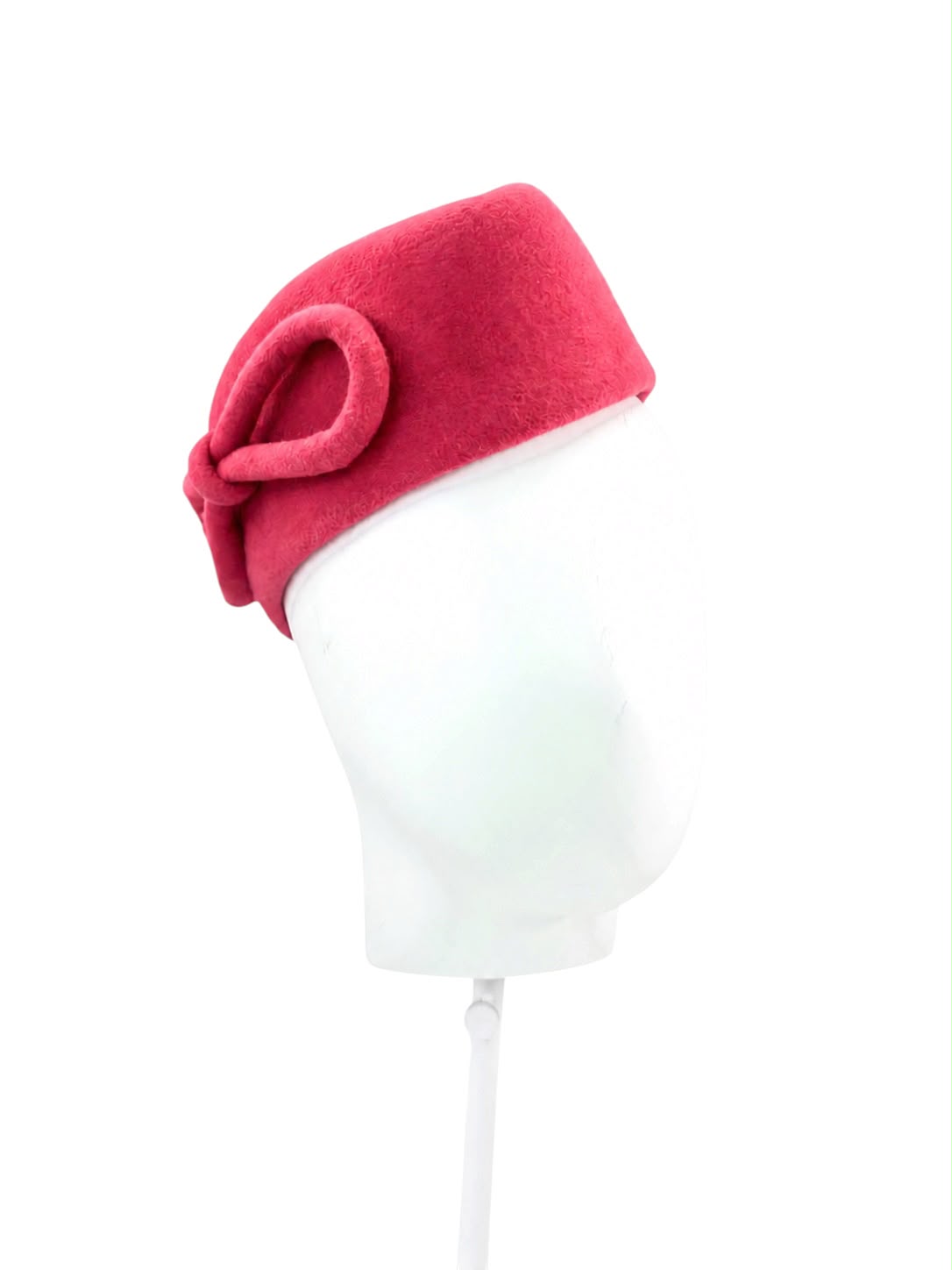 Pink sculptural pillbox hat with a hand-shaped bow worn on a stand, Maria Monica London