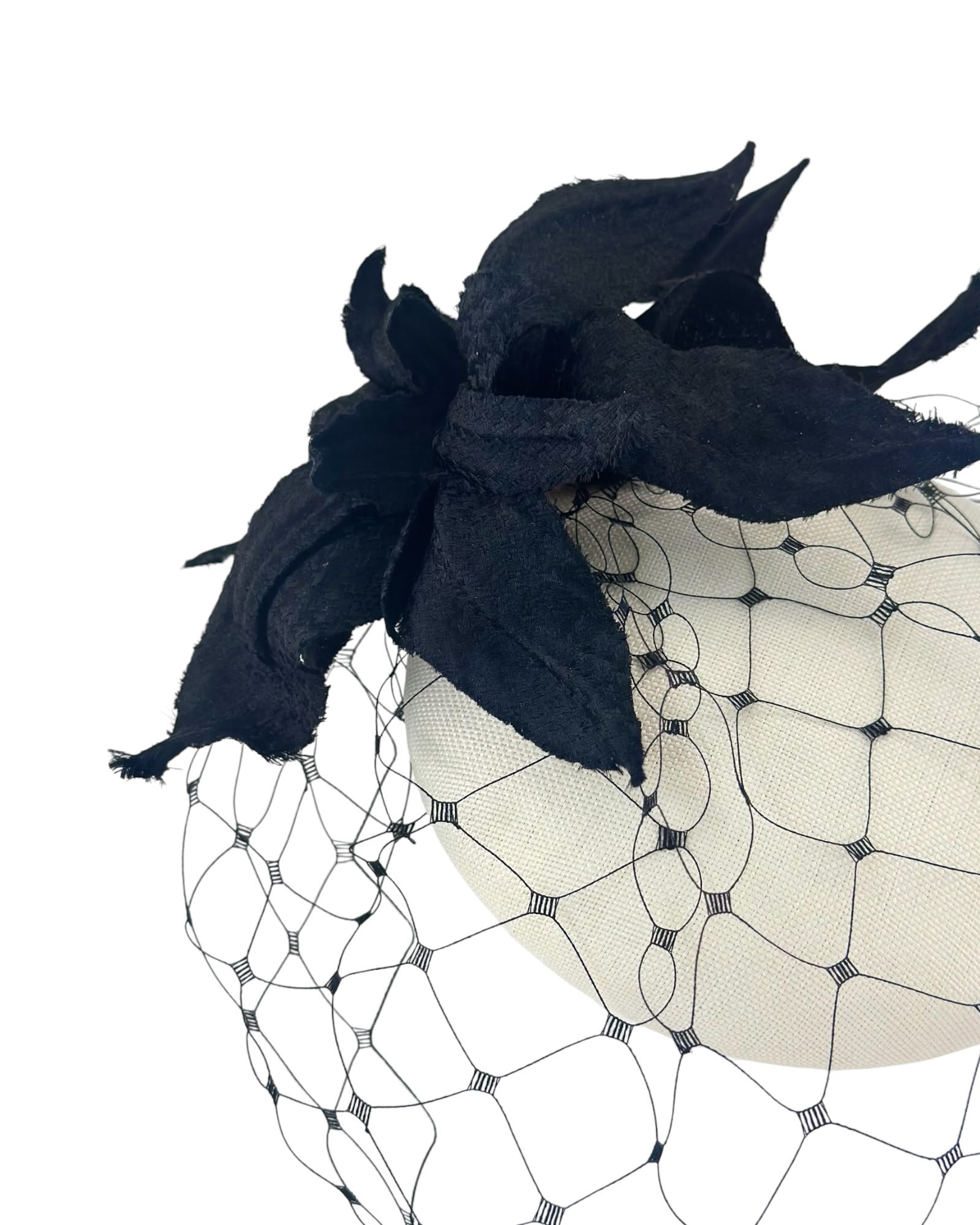Close view of a black raw edged flower and black net veil on an ivory cocktail hat, Maria Monica London