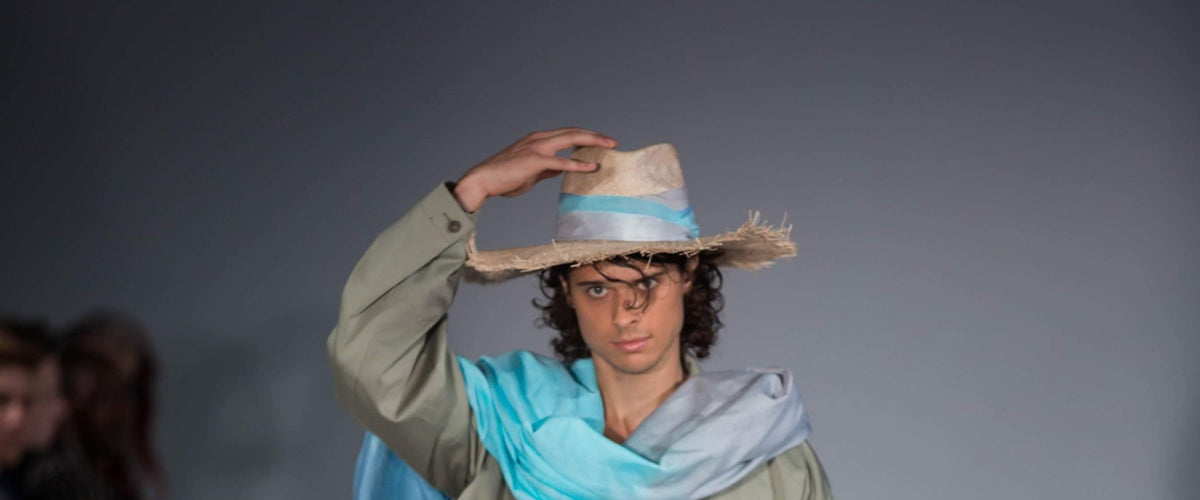 A model on a runway wearing a straw hat with a frayed brim and a pale blue band
